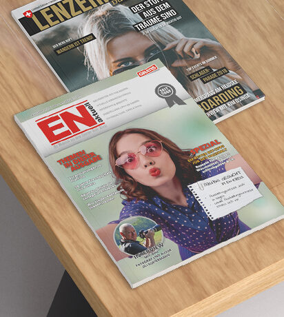 Revistas "Lenzerheide" y "EN Magazine" sobre una mesa de madera, destacando sus portadas coloridas y contenido atractivo.