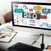 Pantalla de computadora mostrando un diseño creativo sobre SEO, con elementos gráficos como gráficos, íconos de redes sociales y conceptos de contenido, en un entorno de oficina con herramientas de trabajo.